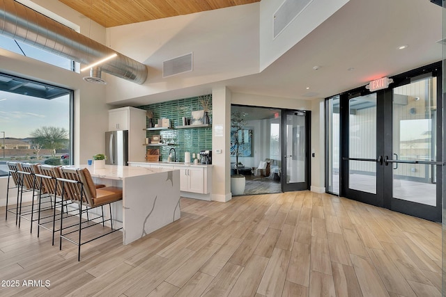 interior space featuring light wood finished floors, freestanding refrigerator, visible vents, and french doors