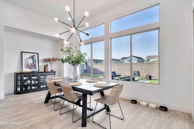 dining space with light wood-style floors, a chandelier, a high ceiling, and baseboards