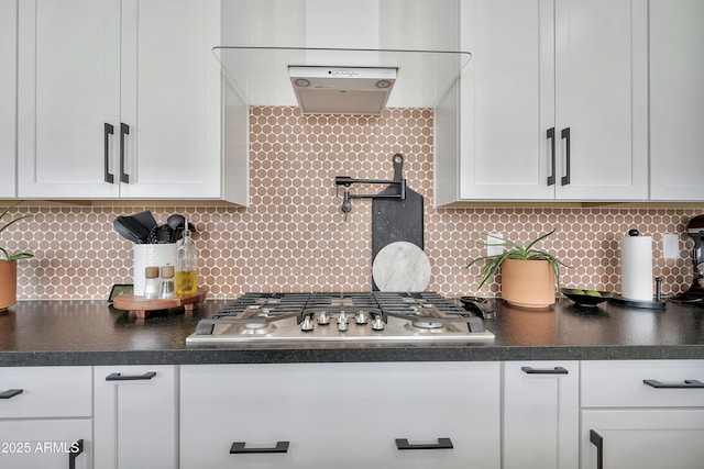 kitchen with dark countertops, white cabinets, stainless steel gas stovetop, and backsplash