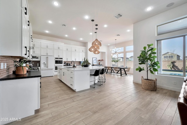 kitchen with built in appliances, a breakfast bar area, a sink, white cabinetry, and light wood finished floors