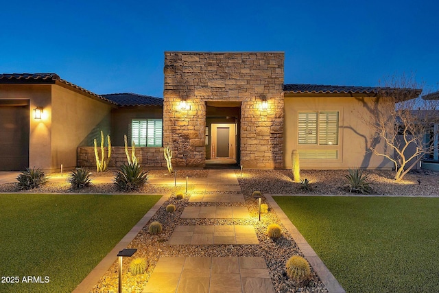 doorway to property featuring stone siding, a lawn, a tile roof, and stucco siding