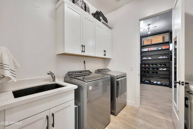 clothes washing area with a sink, baseboards, washer and dryer, light wood-type flooring, and cabinet space