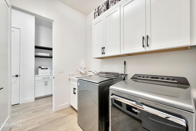 laundry room featuring cabinet space, baseboards, washer and clothes dryer, and light wood finished floors