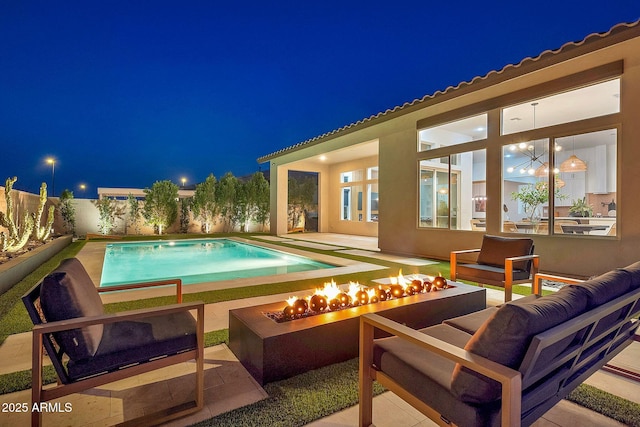 pool at night featuring a fenced in pool, an outdoor living space with a fire pit, a patio, and a fenced backyard