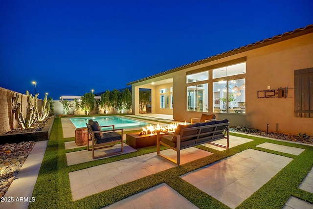 patio at night featuring a fenced in pool, an outdoor living space with a fire pit, and a fenced backyard