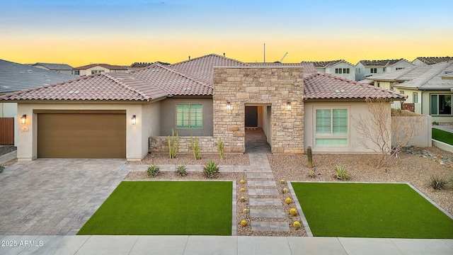 mediterranean / spanish home featuring an attached garage, a tile roof, stone siding, driveway, and stucco siding