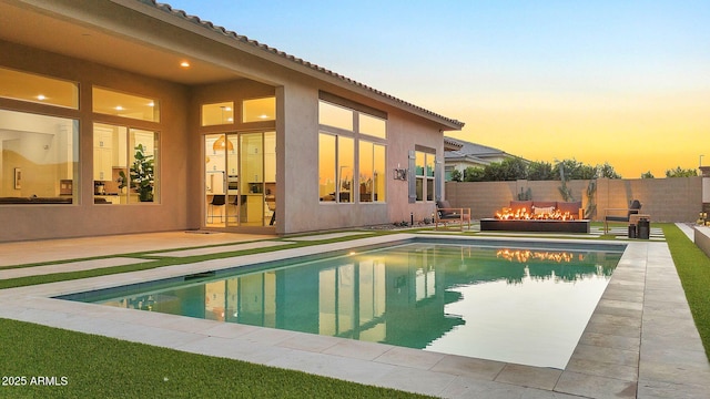 pool at dusk with an outdoor fire pit, a patio area, fence, and a fenced in pool