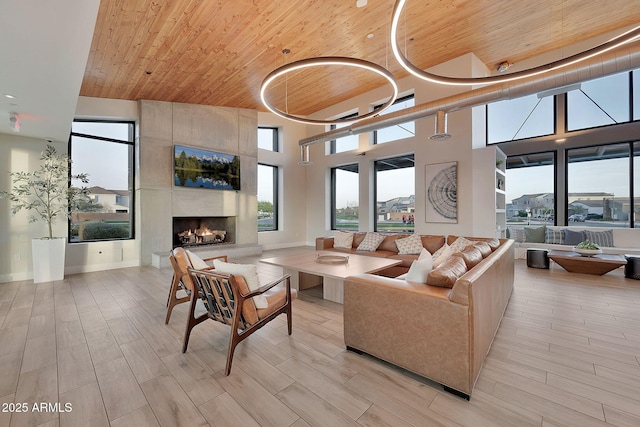 living room with wood finish floors, a towering ceiling, a tile fireplace, wooden ceiling, and baseboards