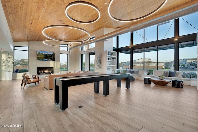 recreation room with a tile fireplace, wooden ceiling, wood finish floors, and a high ceiling