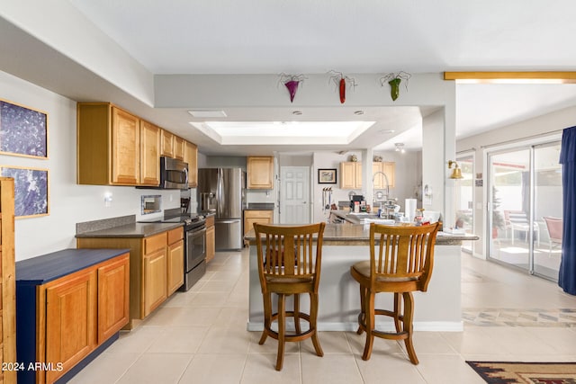 kitchen featuring a kitchen breakfast bar, light tile patterned floors, a raised ceiling, and stainless steel appliances