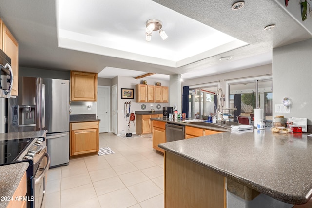 kitchen with stainless steel appliances, a raised ceiling, light tile patterned flooring, light brown cabinetry, and a textured ceiling