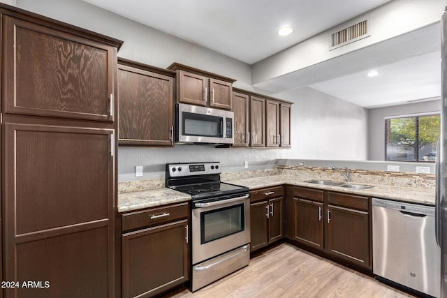 kitchen with light stone countertops, dark brown cabinetry, stainless steel appliances, sink, and light hardwood / wood-style floors