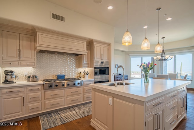 kitchen with decorative light fixtures, an island with sink, sink, dark hardwood / wood-style flooring, and stainless steel gas cooktop