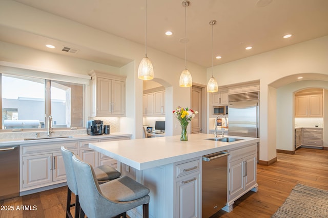 kitchen featuring built in appliances, sink, pendant lighting, and an island with sink