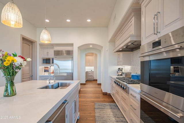 kitchen featuring built in appliances, sink, decorative light fixtures, and white cabinets