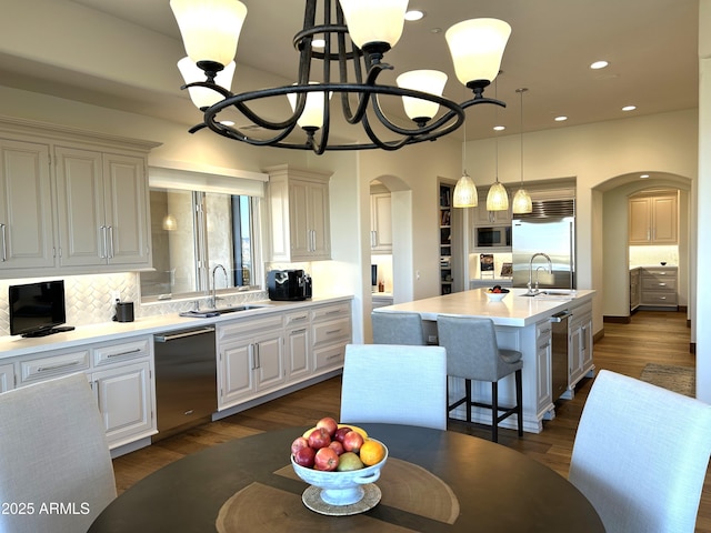 kitchen featuring sink, an inviting chandelier, built in appliances, an island with sink, and decorative light fixtures