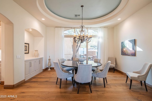 dining area with a tray ceiling, a chandelier, and light wood-type flooring