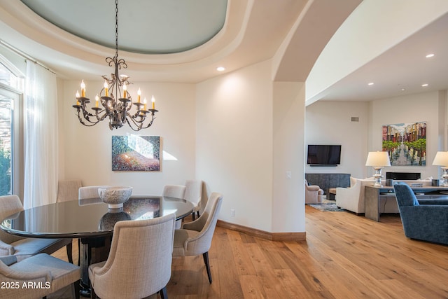 dining area with a raised ceiling, an inviting chandelier, and light hardwood / wood-style flooring