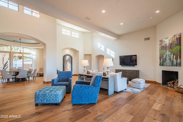 living room with a notable chandelier, hardwood / wood-style flooring, and a towering ceiling