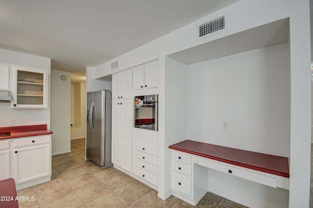 kitchen featuring white cabinets, light tile patterned flooring, stainless steel appliances, and a textured ceiling