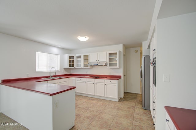 kitchen featuring kitchen peninsula, sink, stovetop, white cabinets, and stainless steel refrigerator