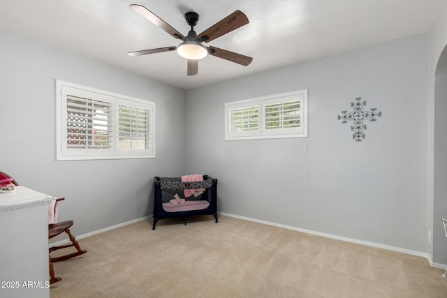 sitting room featuring ceiling fan, arched walkways, light carpet, and baseboards