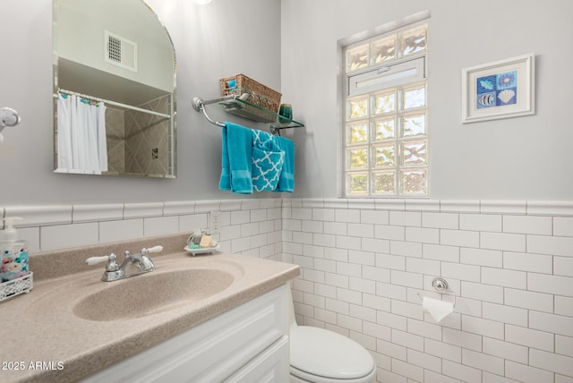 full bathroom featuring tile walls, vanity, toilet, curtained shower, and a wainscoted wall