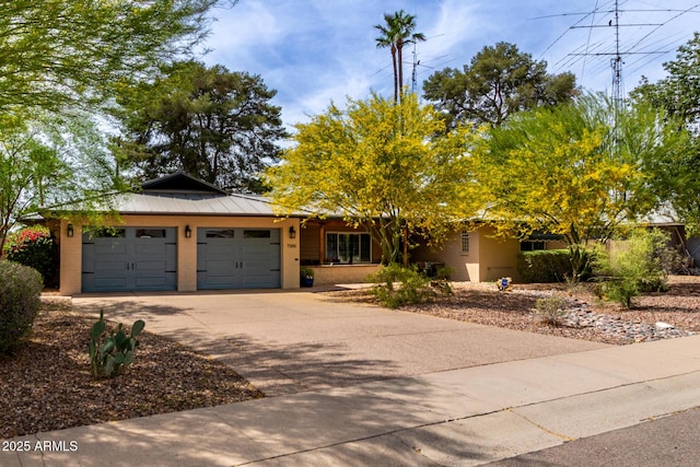ranch-style house with an attached garage, concrete driveway, a standing seam roof, metal roof, and stucco siding