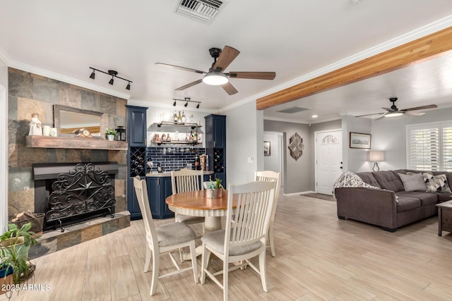dining space with a ceiling fan, a fireplace, crown molding, light wood-style floors, and baseboards