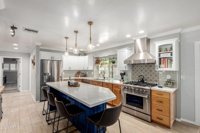kitchen with stainless steel appliances, wall chimney range hood, a sink, a center island, and a kitchen breakfast bar