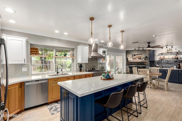 kitchen featuring appliances with stainless steel finishes, tasteful backsplash, a sink, wall chimney range hood, and a kitchen island