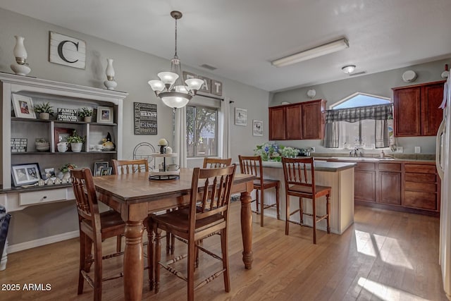 dining space with sink, plenty of natural light, light wood-type flooring, and an inviting chandelier