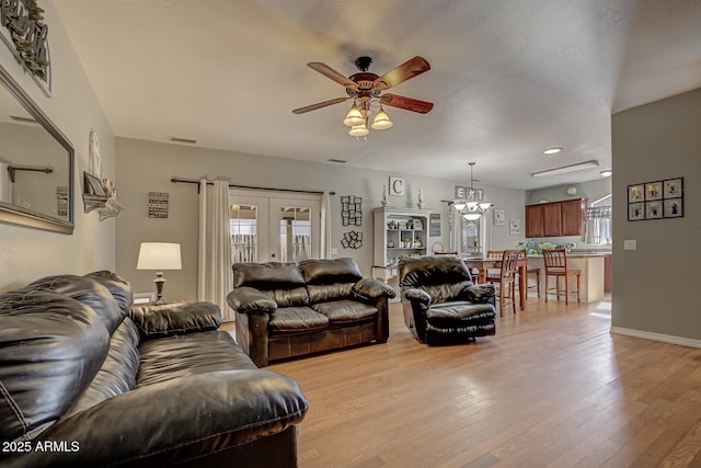 living room featuring ceiling fan with notable chandelier, french doors, and light wood-type flooring