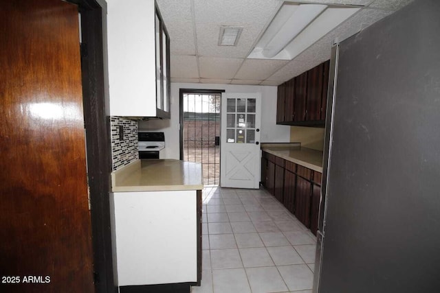 kitchen featuring dark brown cabinetry, tasteful backsplash, light tile patterned floors, and stainless steel refrigerator