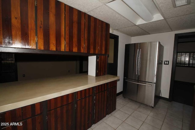 kitchen with a paneled ceiling, light tile patterned floors, and stainless steel fridge