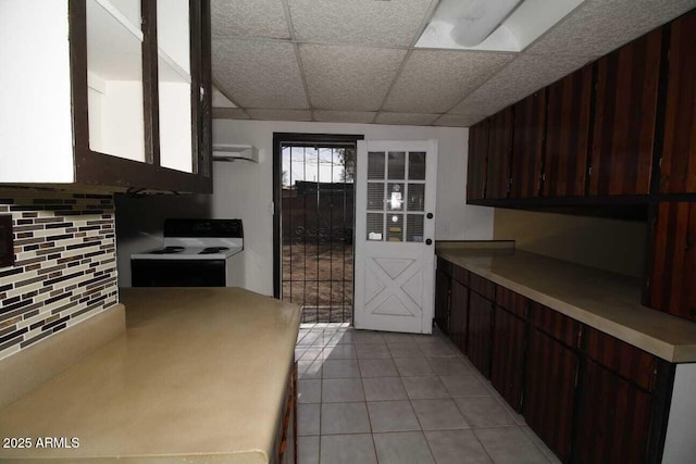 kitchen with light tile patterned flooring, a paneled ceiling, dark brown cabinets, range with electric stovetop, and backsplash