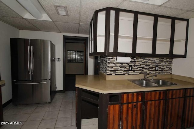 kitchen featuring sink, stainless steel fridge, a paneled ceiling, light tile patterned flooring, and decorative backsplash