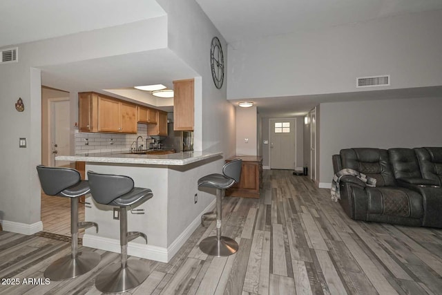 kitchen with light wood-style floors, visible vents, backsplash, and a kitchen bar