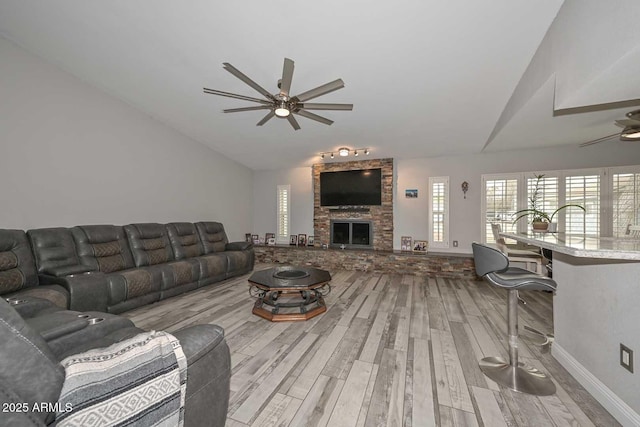 living room with a stone fireplace, vaulted ceiling, a ceiling fan, and wood finished floors