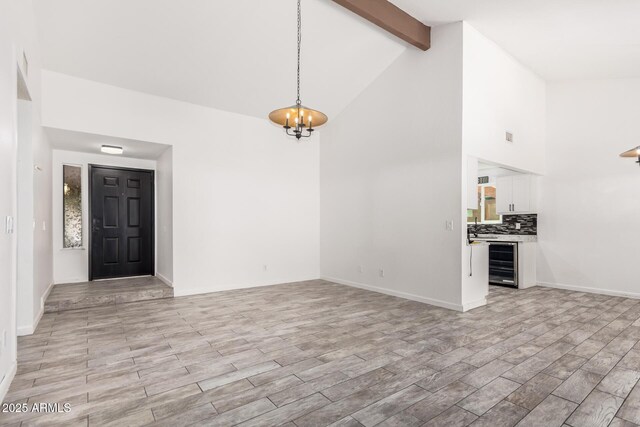 2109 E Gelding Dr, Phoenix, AZ 85022 - unfurnished living room with wine cooler, beam ceiling, a chandelier, high vaulted ceiling, and light wood-style floors