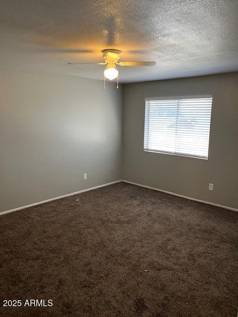 empty room with baseboards, dark carpet, and a ceiling fan