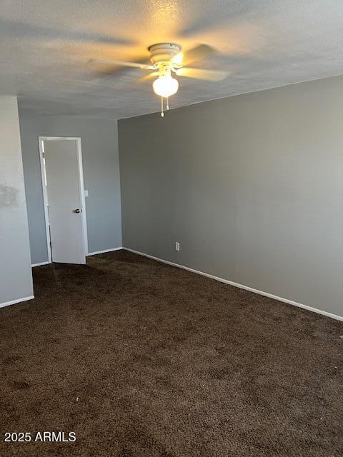 empty room featuring dark colored carpet, ceiling fan, a textured ceiling, and baseboards