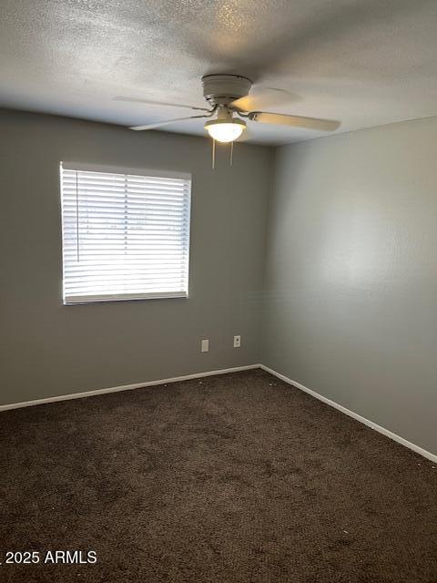 unfurnished room with dark carpet, a textured ceiling, baseboards, and ceiling fan