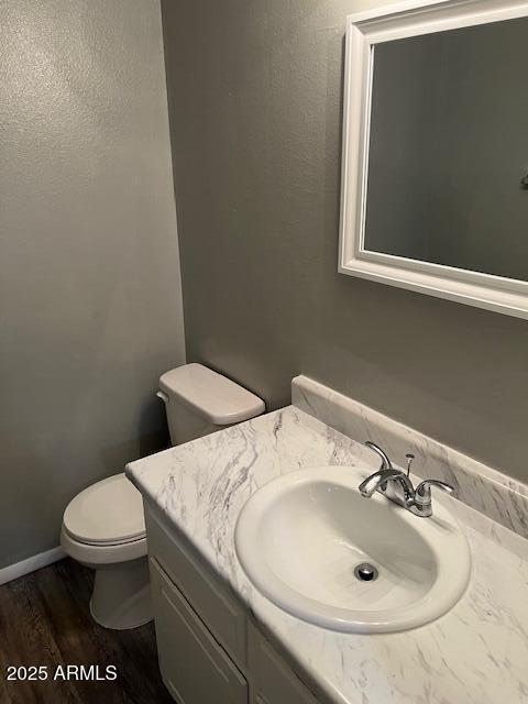 half bath featuring baseboards, vanity, toilet, and wood finished floors