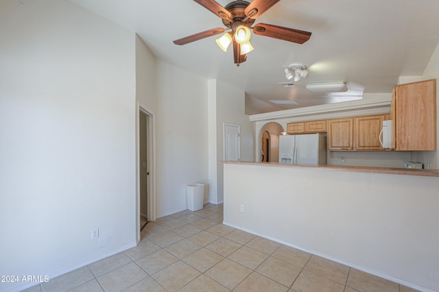 interior space featuring light brown cabinets, kitchen peninsula, ceiling fan, light tile patterned floors, and white appliances