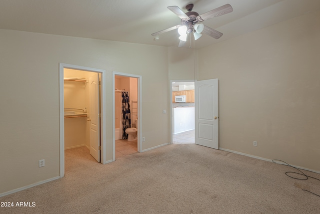 unfurnished bedroom featuring light carpet, ceiling fan, a closet, ensuite bathroom, and a walk in closet