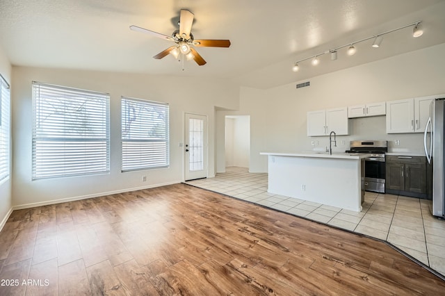 kitchen featuring white cabinetry, vaulted ceiling, an island with sink, stainless steel appliances, and light hardwood / wood-style floors