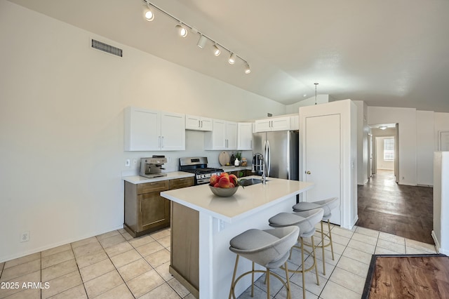 kitchen featuring vaulted ceiling, light tile patterned floors, stainless steel appliances, a kitchen island with sink, and white cabinets