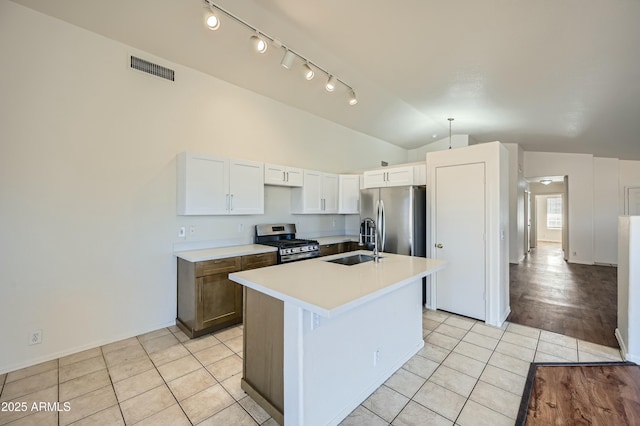 kitchen with lofted ceiling, white cabinetry, light tile patterned floors, appliances with stainless steel finishes, and an island with sink