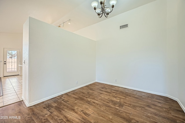 unfurnished room with hardwood / wood-style flooring, rail lighting, a chandelier, and vaulted ceiling